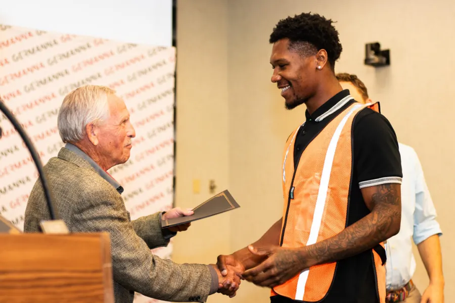 A participant in a safety vest shakes hands at the Infrastructure of the Internet Pre-Apprenticeship